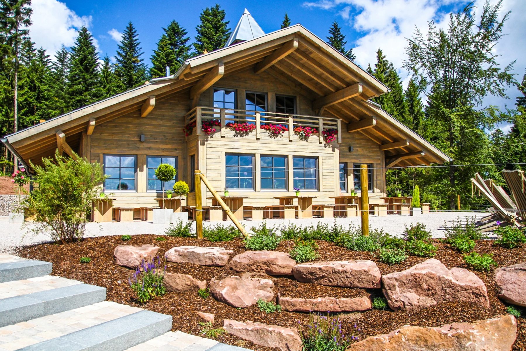 Die Berghütte Lauterbad im Sommer: Holzhaus mit Blumenbalkon und Terrasse zwischen hohen Tannen